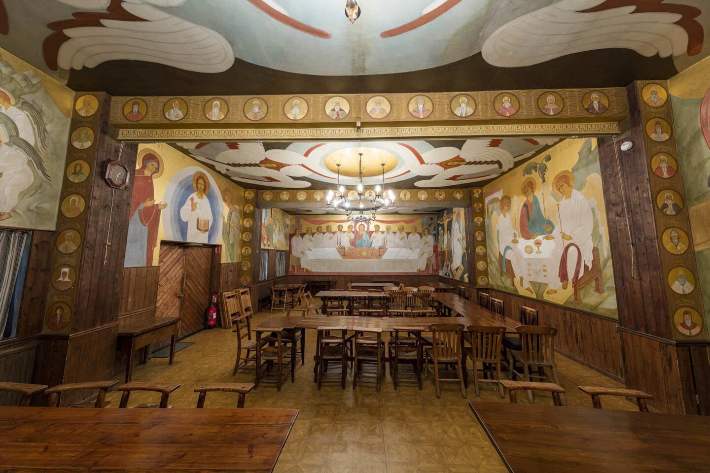 Artistic dining hall with religious murals and wooden tables