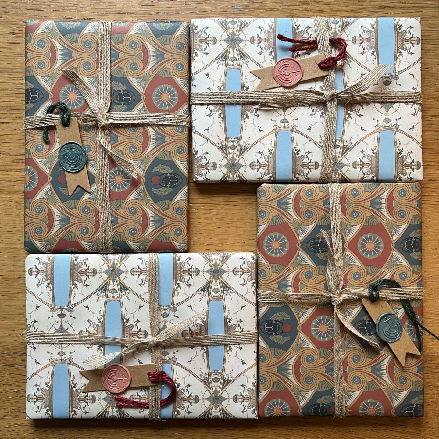 Four wrapped gifts with ornate patterned paper and twine, on a wooden surface.