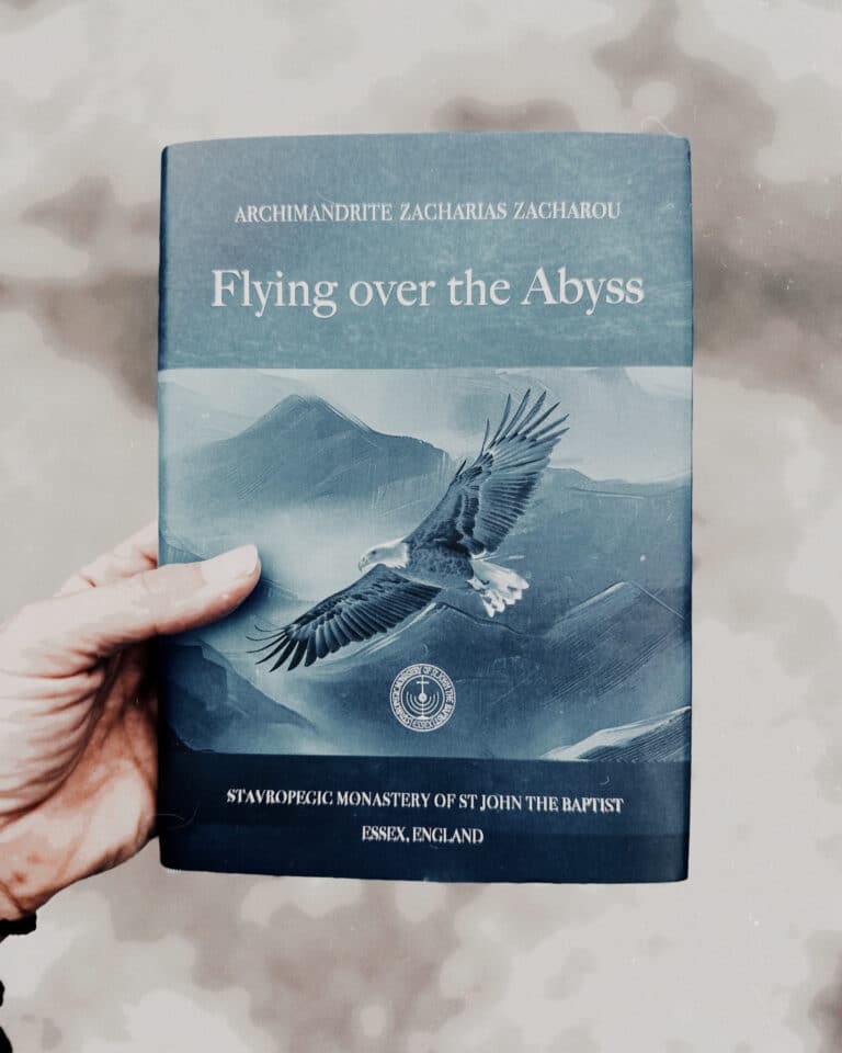 Hand holding a book titled "Flying Over the Abyss" by Zacharias Zacharos