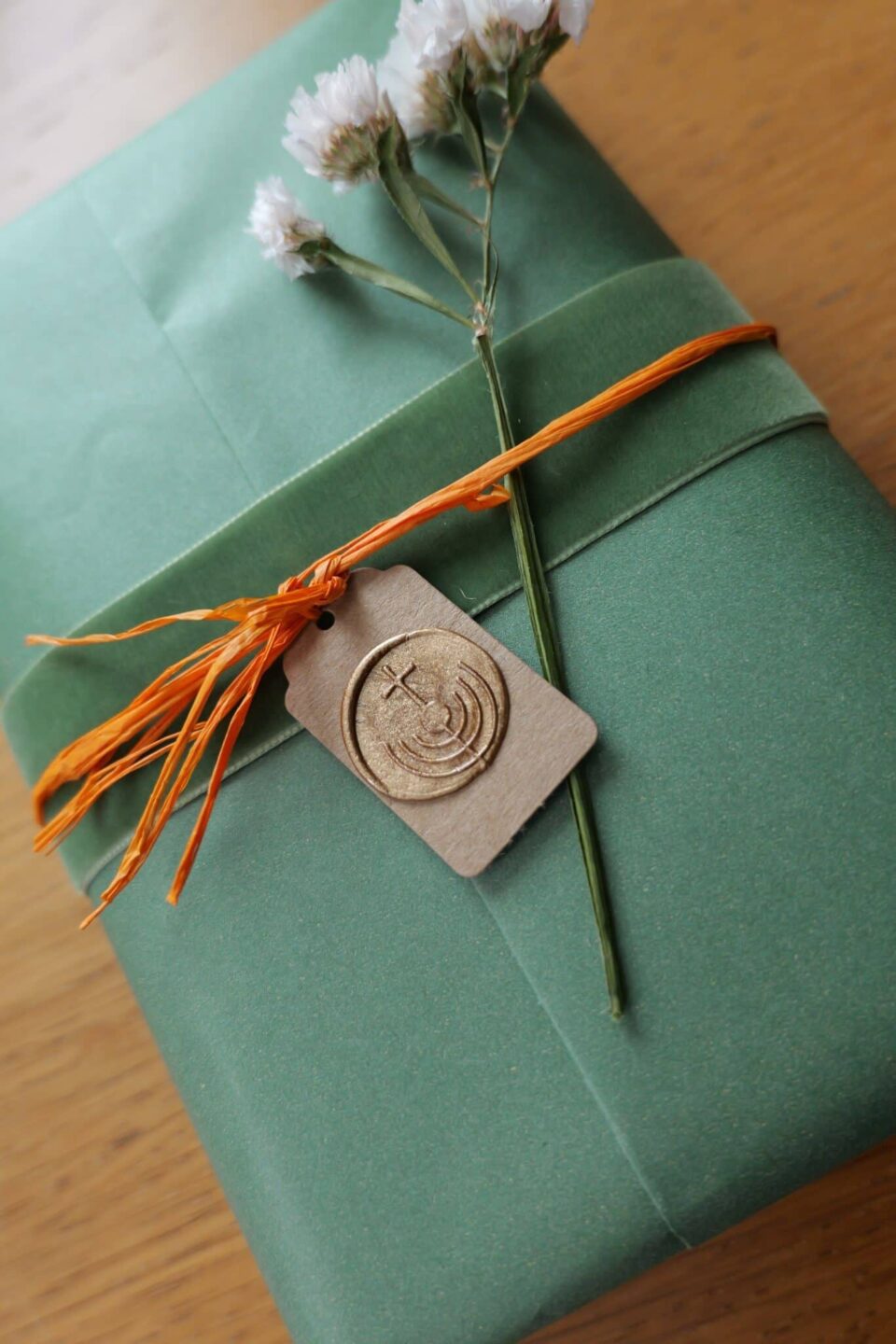 Green gift wrap with orange ribbon, dried flowers, and wax seal tag
