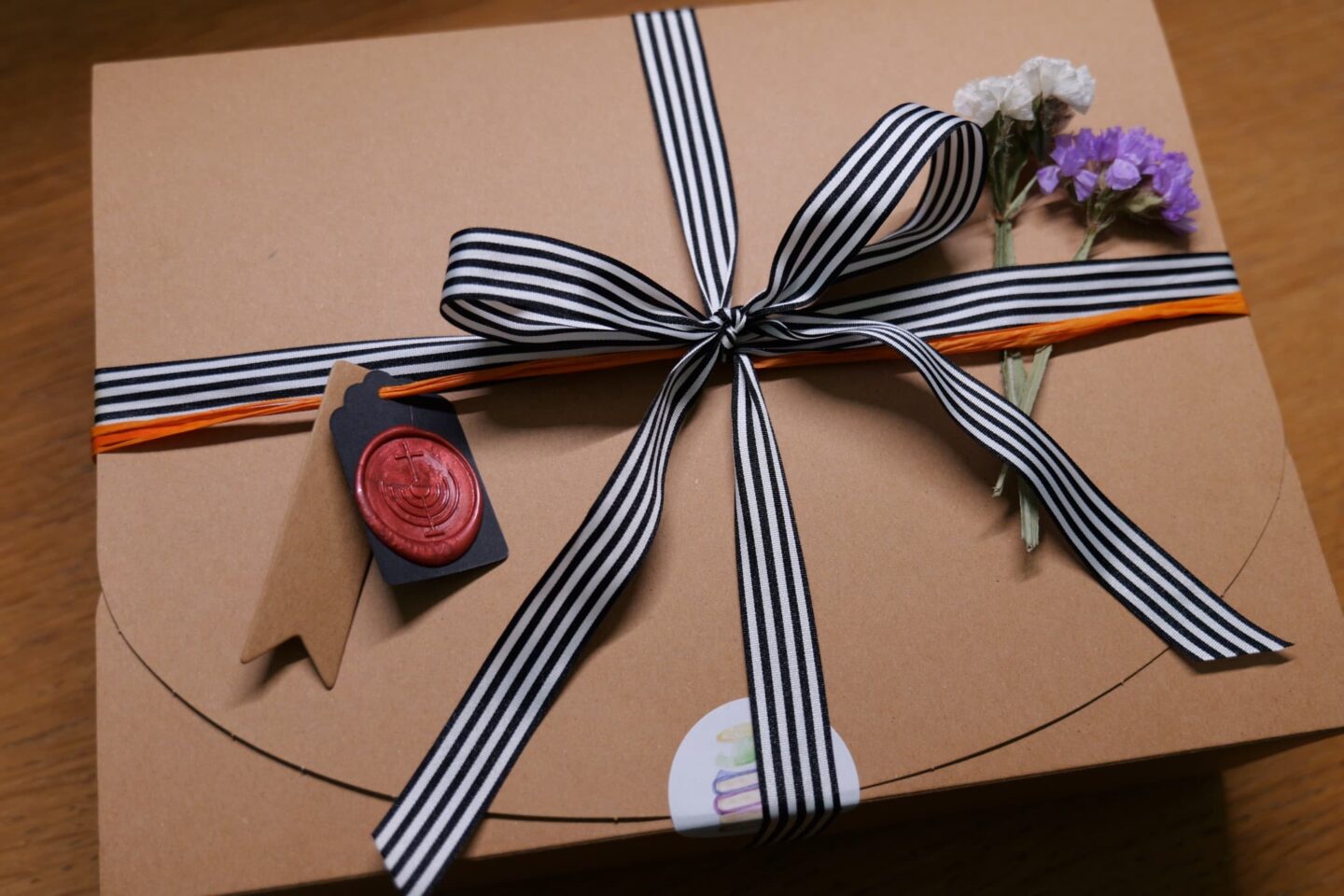 Brown gift box with black and white striped ribbon, wax seal, and dried flowers