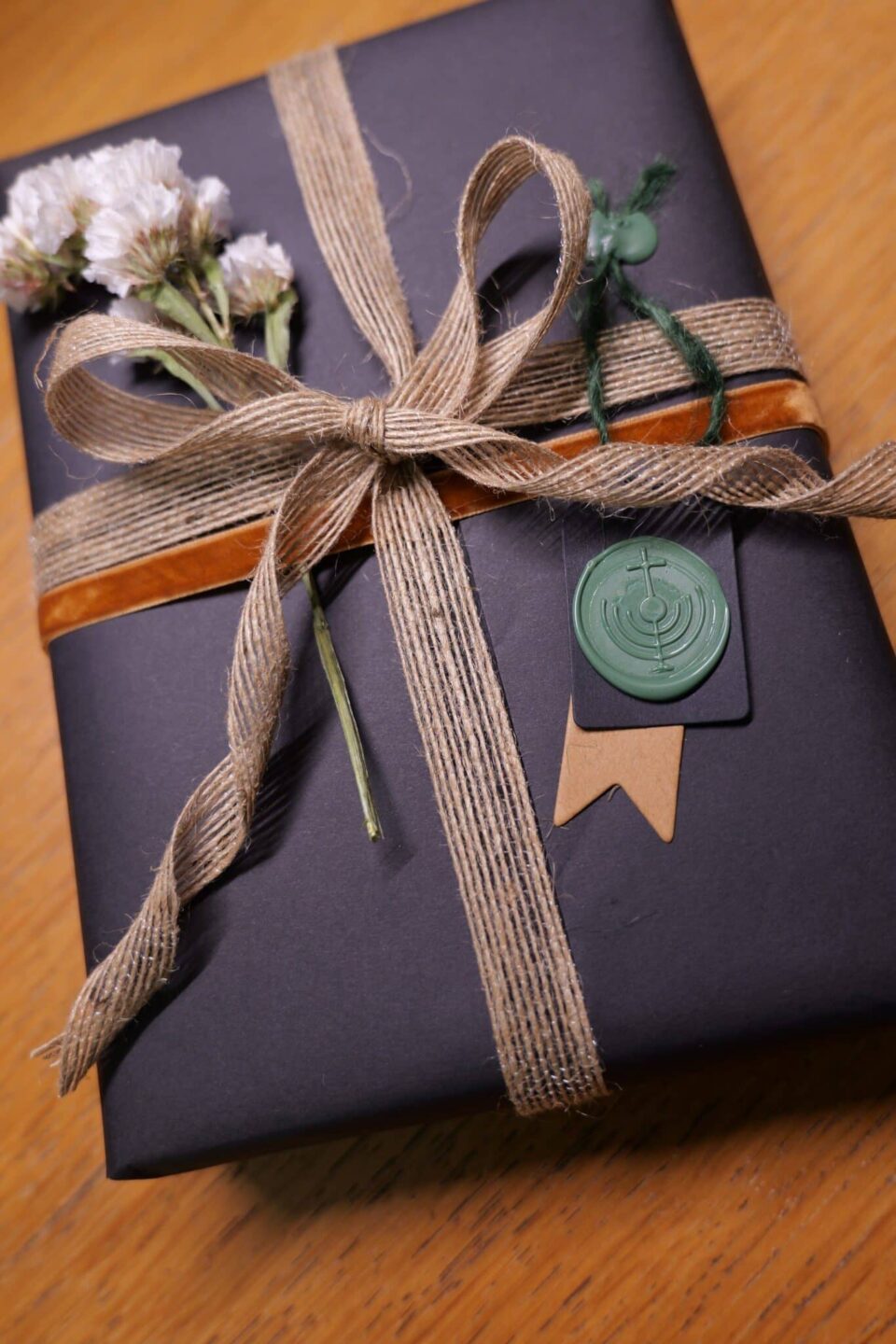 Gift-wrapped book in black paper with twine, dried flowers, and wax seal