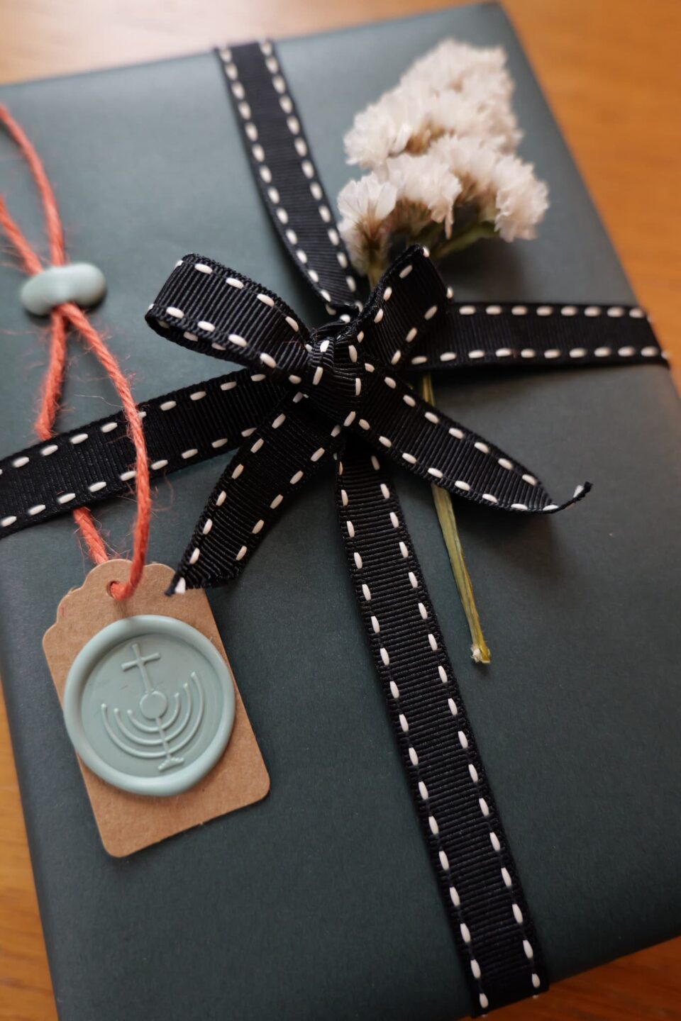 Dark green gift box with black ribbon, dried flower, and teal wax seal tag