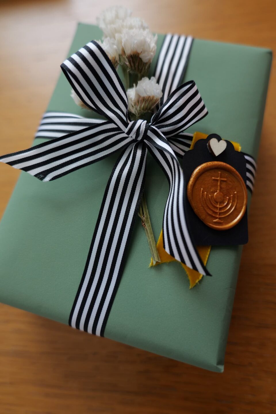 Gift-wrapped present with black and white striped ribbon, dried flowers, and menorah wax seal