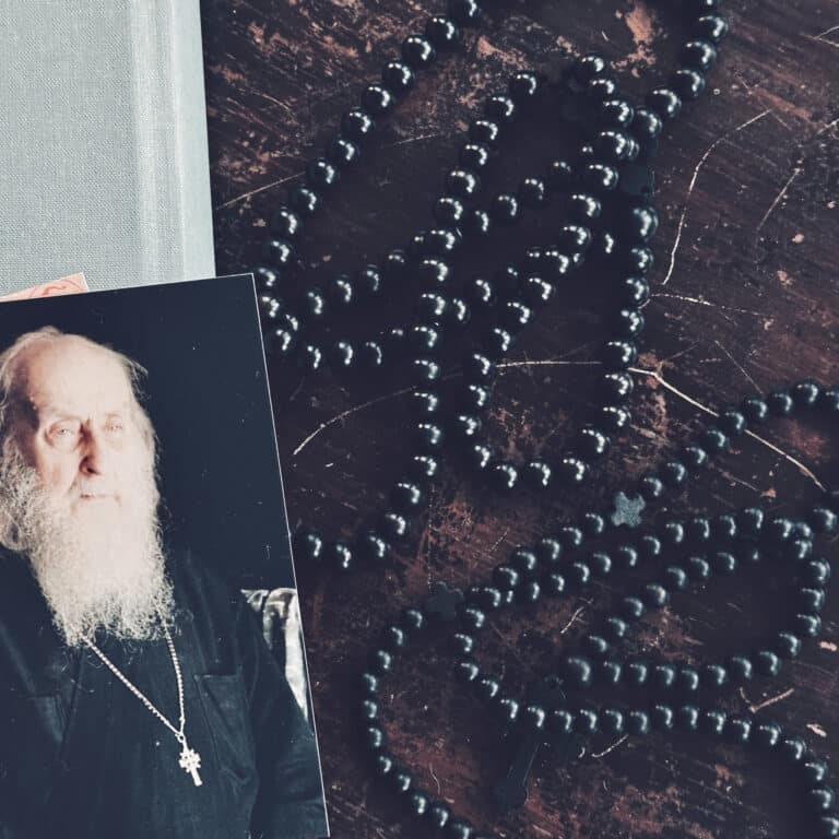 Elderly Orthodox priest with white beard and black cassock, prayer beads on wooden table