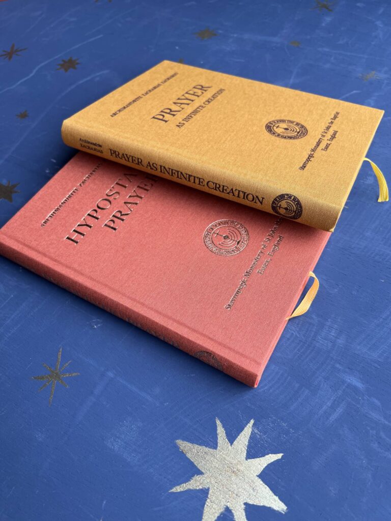 Two books, "Prayer As Infinite Creation" and "Hypostase Prayer," stacked on a blue surface.